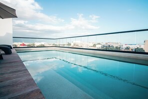 Ein Pool auf dem Dach mit klarem, blauem Wasser, einer Holzterrasse und einem Stadtblick im Hintergrund.