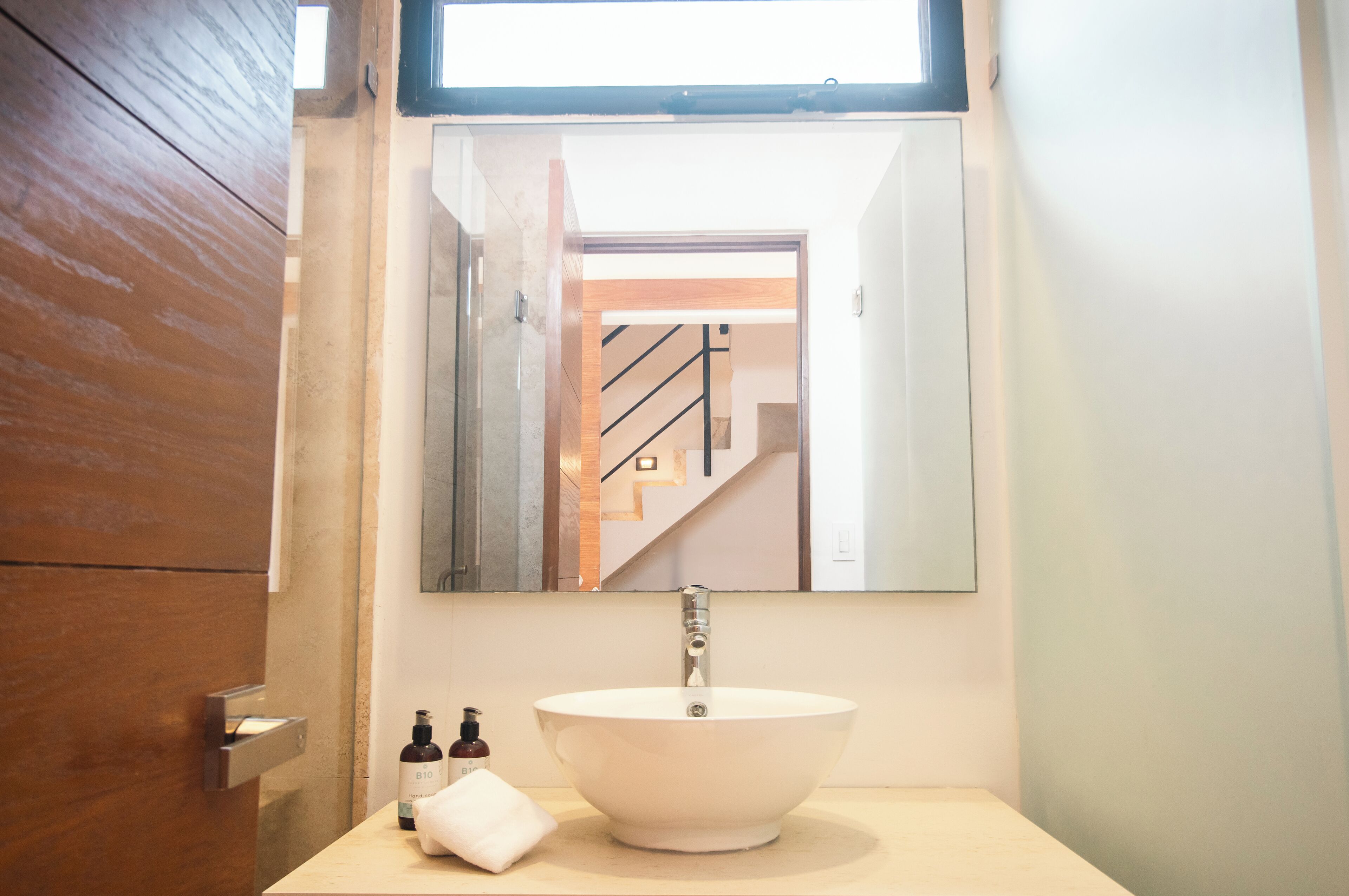 A bathroom with a white sink, a mirror, and a bottle of hand soap.