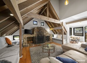 Un acogedor dormitorio tipo loft con chimenea de piedra, vigas de madera y un gran ventanal.