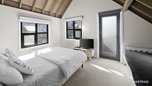 A bedroom with a sloped ceiling, a bed, a desk with a computer, and a door. - Meltwater Chalet (Dinner Plain)