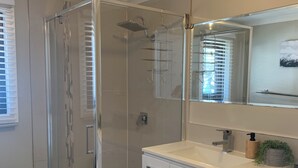 A modern bathroom with a glass-enclosed shower, a white vanity with a sink, and a toilet. - Meltwater Chalet (Dinner Plain)