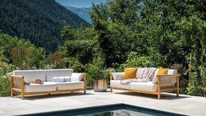 A poolside area with two white sofas and a small table, surrounded by lush greenery and mountains in the background. - Chalet Wonderland - Amazing chalet for 13 with summer pool - OVO Network (Séez)