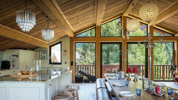 A spacious kitchen with a large island, wooden beams, and large windows offering a view of the outdoors. - Chalet Wonderland - Amazing chalet for 13 with summer pool - OVO Network (Séez)