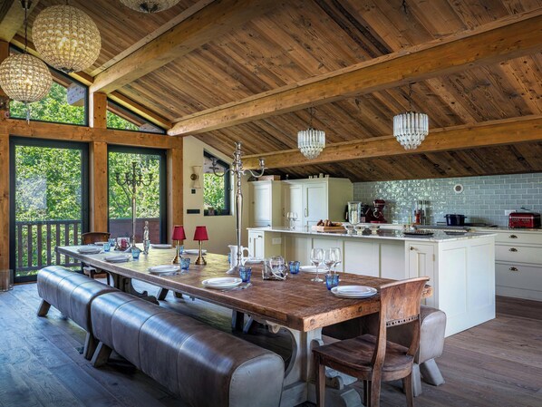 Un comedor de madera con una mesa larga, bancos y candelabros colgantes.