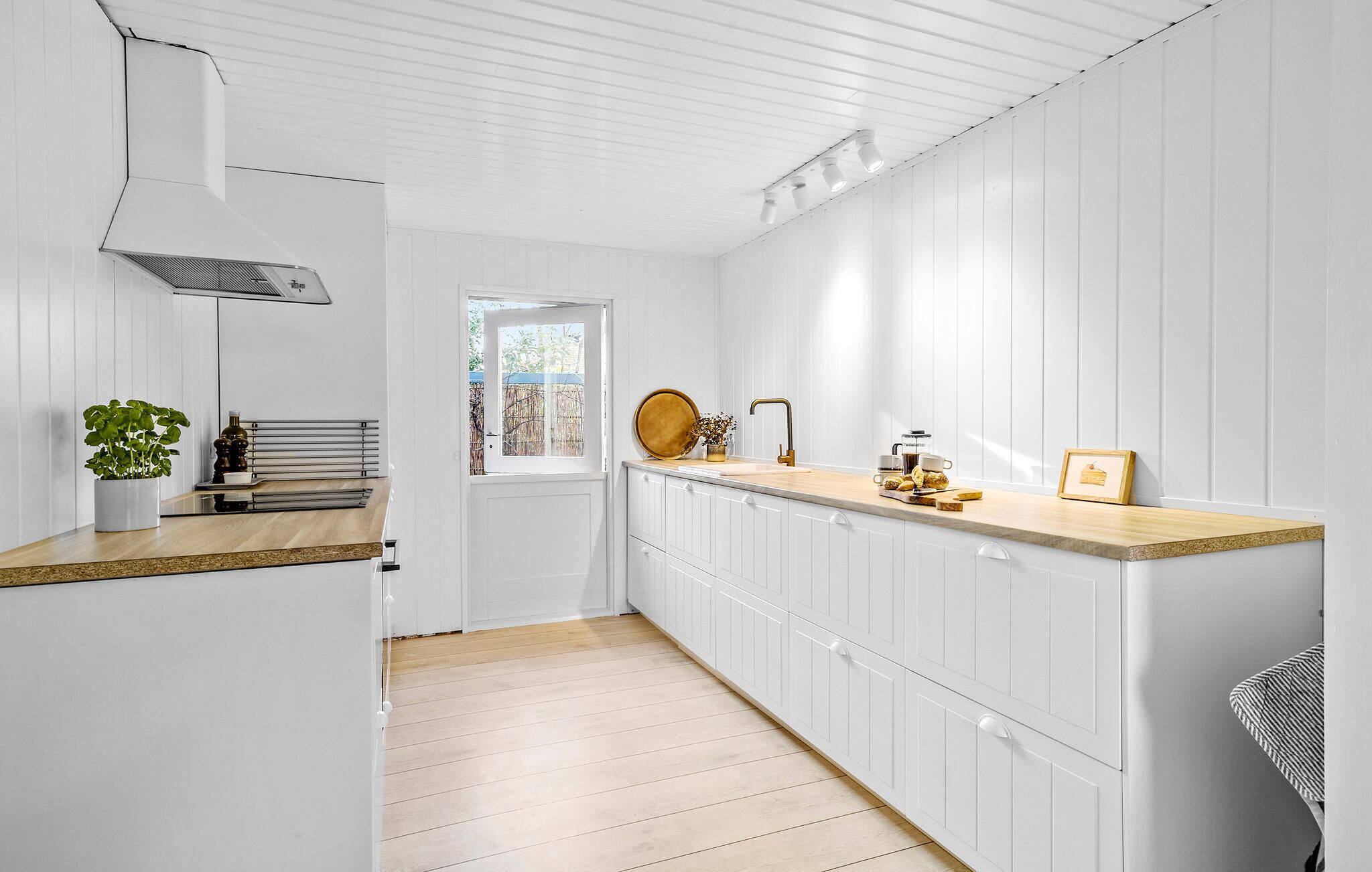 Una cocina con armarios blancos, encimera de madera, una ventana y una planta.