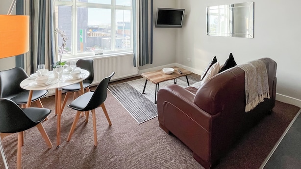 Ein Wohnzimmer mit Esstisch, Stühlen, einer Couch, einem Fernseher und einem Fenster mit Vorhängen.