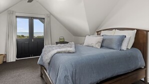 A bedroom with a bed, a ceiling fan, a nightstand, and a view of the outdoors through a door.