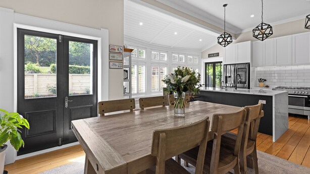 A modern kitchen with a wooden dining table, white cabinets, and a black door.