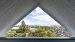 A view from a window with a triangular frame, overlooking a residential area with houses, trees, and a distant body of water.