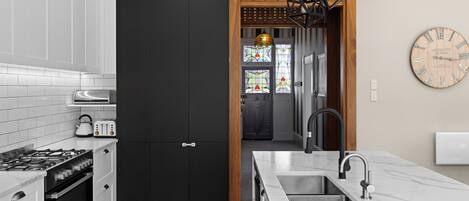 A modern kitchen with white cabinets, a black door, a wooden partition, a hanging light fixture, and a clock on the wall.