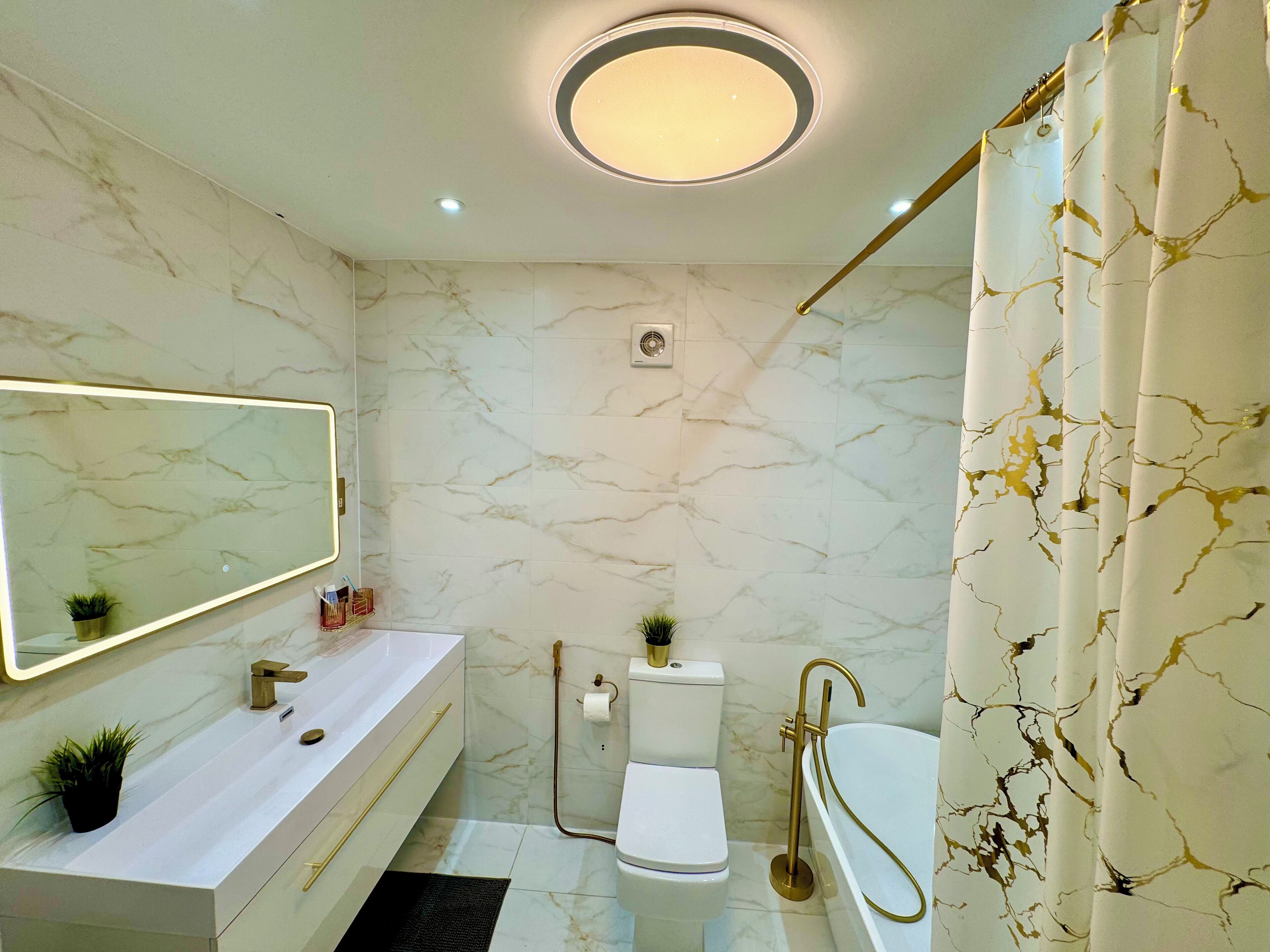 Un bagno con parete in marmo, un mobile lavabo bianco, una vasca dorata e un moderno lampadario.