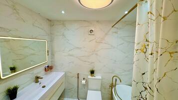 Un bagno con parete in marmo, un mobile lavabo bianco, una vasca dorata e un moderno lampadario.