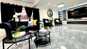 A modern living room with a dark blue sofa, two armchairs, a glass coffee table, and a large flat-screen TV mounted on the wall.