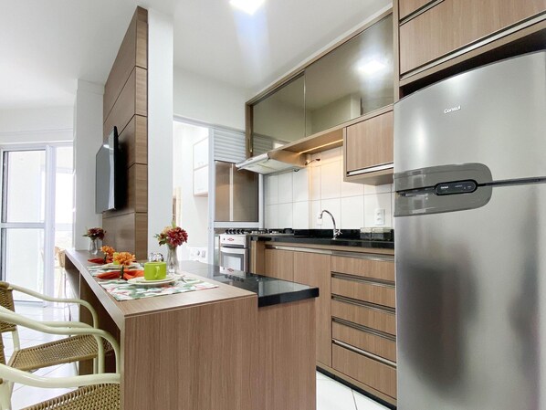 Una cocina moderna con armarios de madera, un refrigerador de acero inoxidable y un comedor con sillas de mimbre.