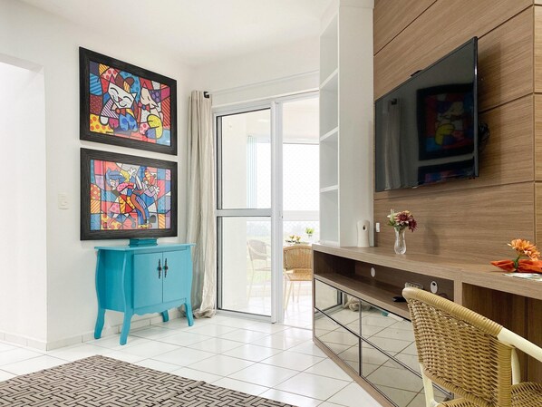 Una sala moderna con un mueble azul, un televisor grande montado en la pared y un sillón de mimbre.