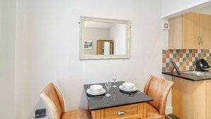Een gezellig eethoekje met een gedekte tafel voor twee, een spiegel boven de tafel en een kitchenette op de achtergrond.