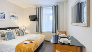 Een hotelkamer met een bed, een bureau met stoel, een flatscreen televisie en twee schilderijen aan de muur.