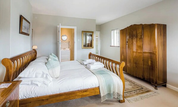 A bedroom with a wooden bed, a wardrobe, and a bathroom visible through an open door.