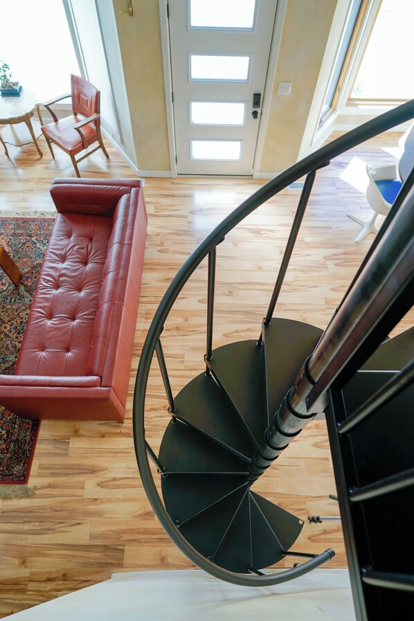 Un escalier en colimaçon avec une rampe en métal noir, un canapé en cuir rouge et un plancher en bois.