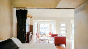 A hotel room with a bed, a red sofa, a coffee table, and a view of the street through an open door. - Style on the Square 2-bedroom bungalow with WiFi, AC in Petersburg (Petersburg)