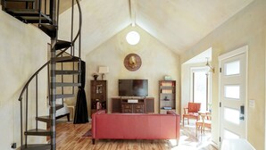 A spacious living room with a wooden floor, a red sofa, a TV, and a spiral staircase. - Style on the Square 2-bedroom bungalow with WiFi, AC in Petersburg (Petersburg)