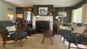 A cozy living room with a fireplace, wooden furniture, and a large window.