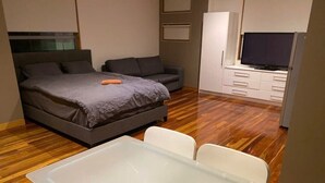 Een slaapkamer met een bed, een bank, een televisie, een kledingkast en een kleine tafel met stoelen.