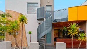 Een modern gebouw met een spiltrap, palmbomen en een gele gevel.