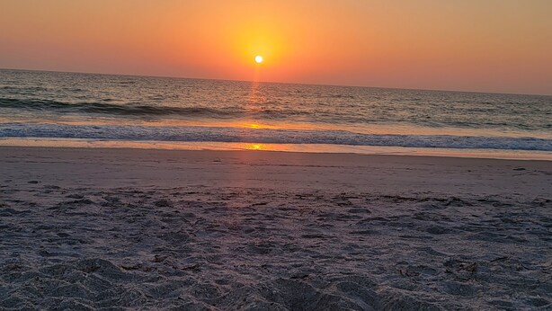 Una playa con el sol poniéndose sobre el océano.