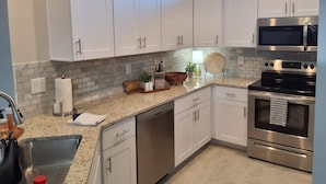 Una cocina moderna con armarios blancos, horno de acero inoxidable y encimera de granito.