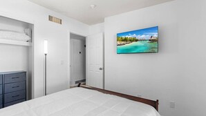 A bedroom with a bed, a wardrobe, a door, and a painting of a beach scene.