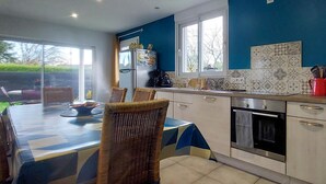 Een moderne keuken met een blauwe accentmuur, een eethoek met rieten stoelen en een groot raam dat voor natuurlijk licht zorgt.