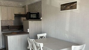A compact kitchen with a microwave, sink, and wooden cabinets. There is a dining area with a table and four chairs. - A practical one-bedroom flat with parking, close to the station and the beach (ARCACHON)