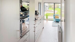 A modern kitchen with white cabinets and stainless steel appliances, leading to a patio with a blue chair and a view of a garden. - 3 bedroom lovely (sta)caravan in Grou (Grou)