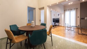A dining area with a round table and chairs, a kitchen in the background, and a living area with a TV. - Acropolis View 3-Bdrm with Rooftop Garden & Jacuzzi (Athens)