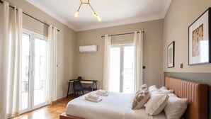 A bedroom with a bed, a desk, and a chair. There is a window with curtains, a ceiling light, and a wall-mounted air conditioner. - Acropolis View 3-Bdrm with Rooftop Garden & Jacuzzi (Athens)