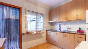 Eine Küche mit Holzausstattung, einem Fenster mit Metallgitter und einem Fliesenboden.