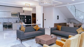 Een moderne keuken met een ingebouwde oven en magnetron, een eethoek met een houten tafel en stoelen, en een woonkamer met een grijze bank en salontafel.
