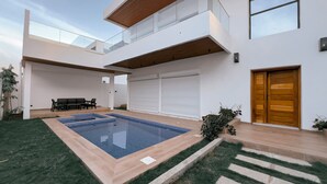 Een modern huis met een zwembad, een houten deur en een balkon.