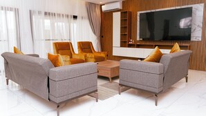Een moderne woonkamer met grijze banken, een salontafel en een grote flatscreen televisie aan de wand.