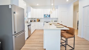 A modern kitchen with white cabinetry, a central island, and a stainless steel refrigerator. - Urban Delight 4br/3ba Near City Center (San Antonio)
