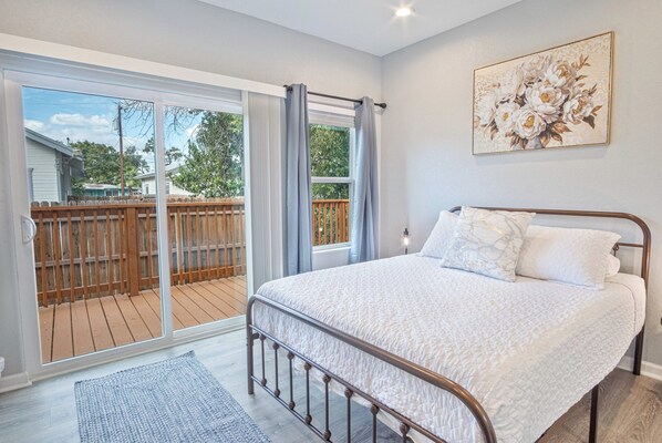 Un dormitorio con una cama grande, un ventanal corredero a una terraza y un cuadro floral en la pared.