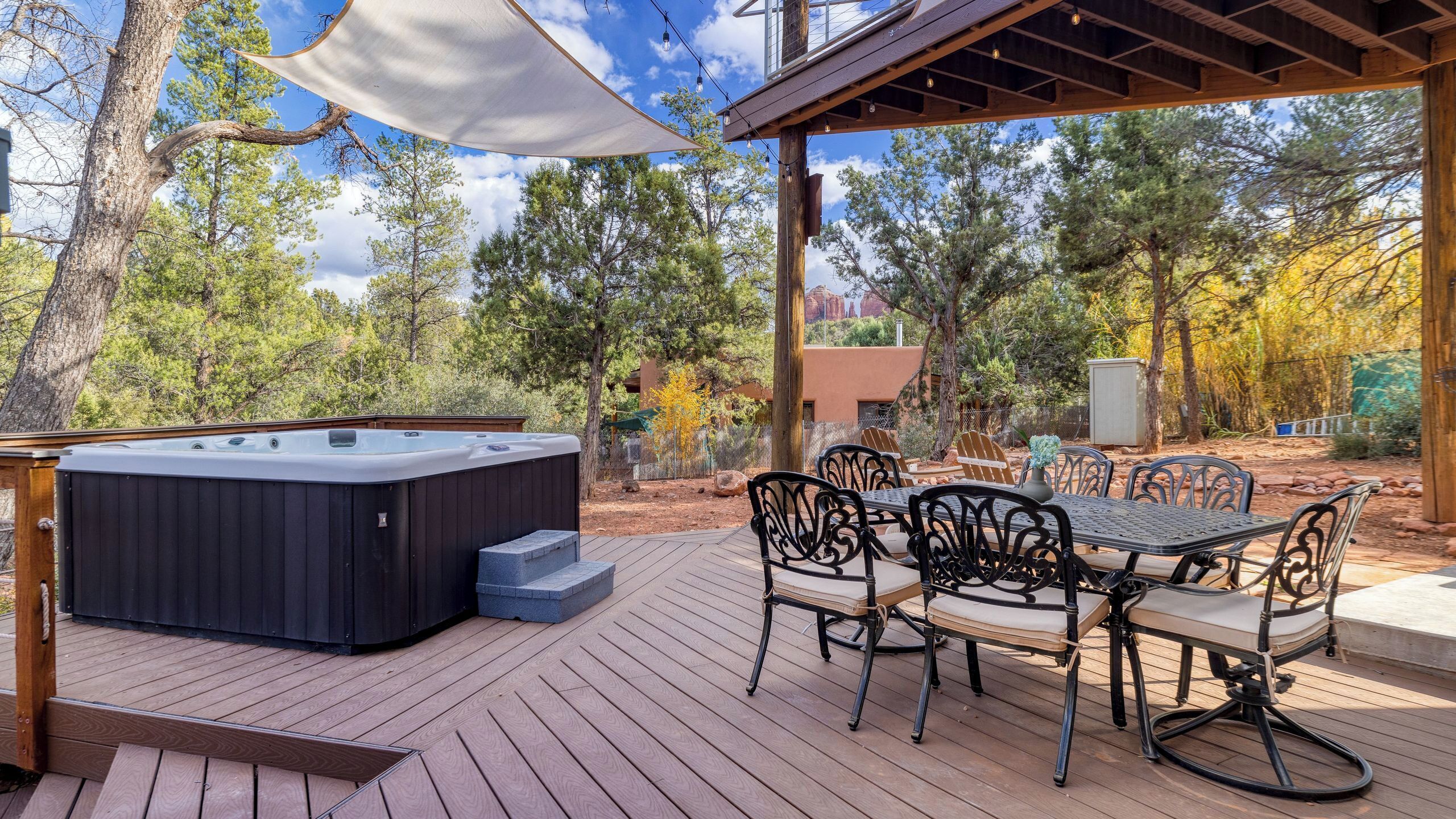 Un jacuzzi, mesa y sillas al aire libre sobre una terraza de madera con una pérgola.