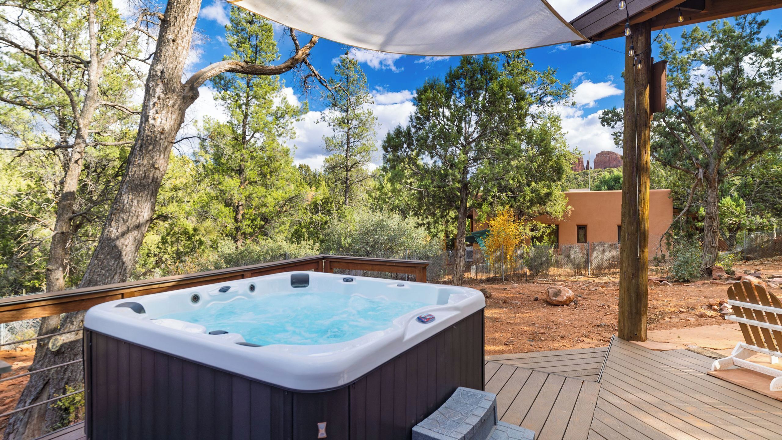 Een hottub op een houten terras, met uitzicht op bomen en een gebouw op de achtergrond.