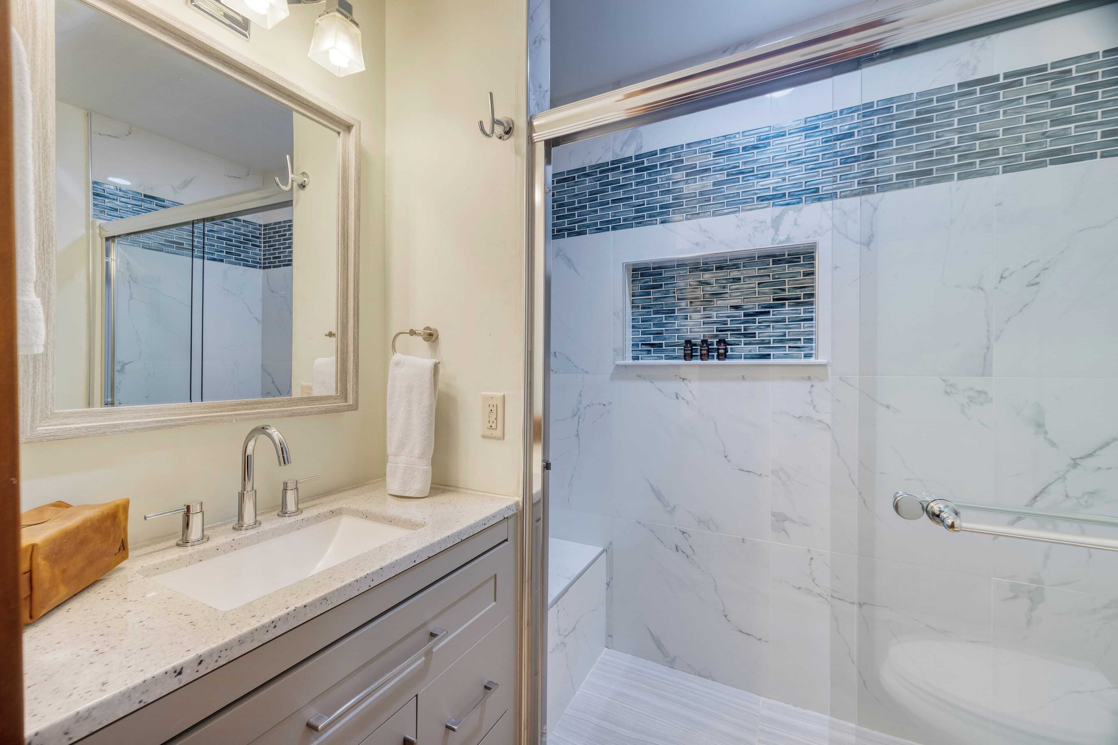 A bathroom with a marble sink, a glass shower enclosure, and a mirror with a towel hanging on the wall.