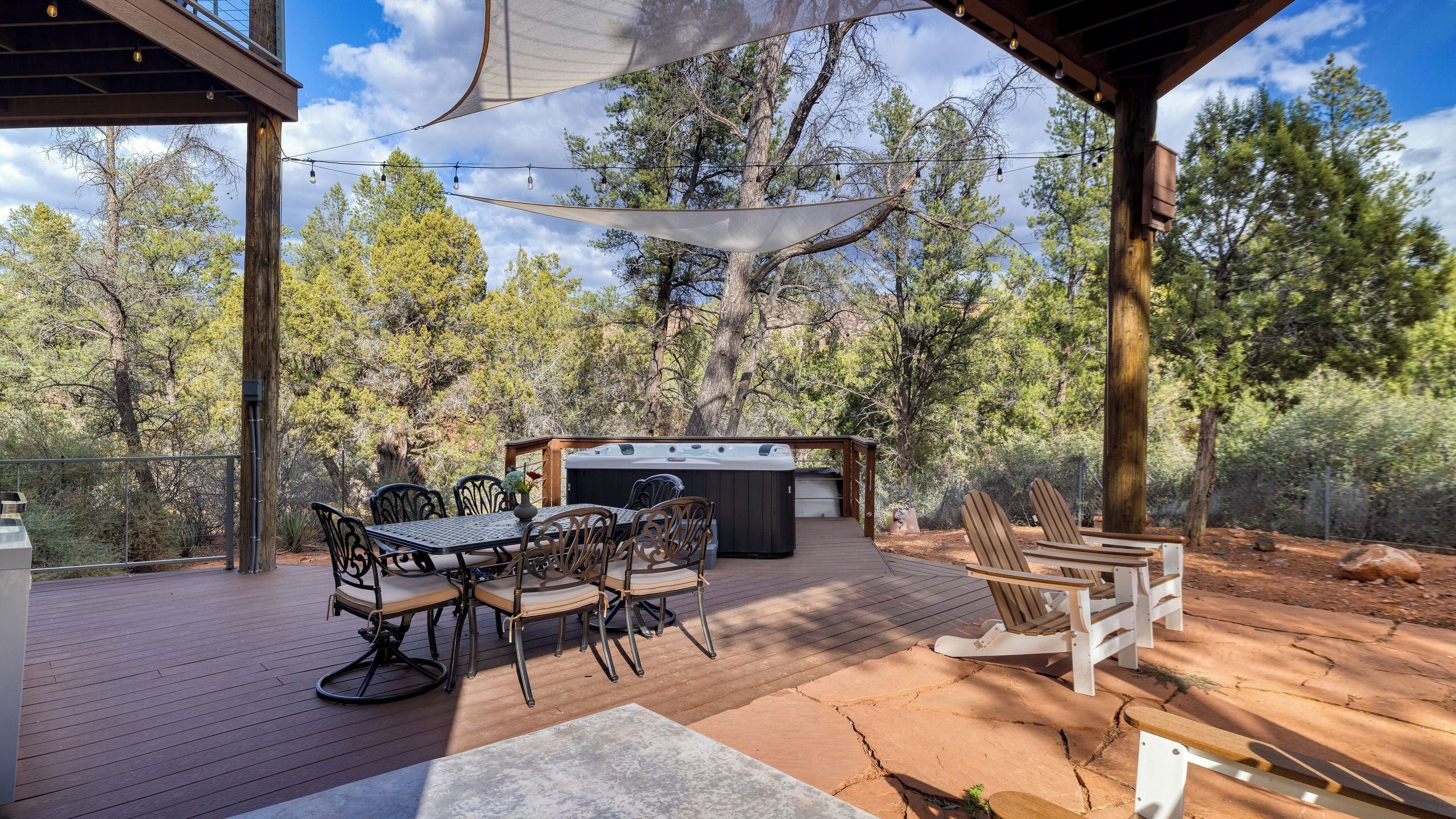 An outdoor deck with a table and chairs, a hot tub, and wooden Adirondack chairs.