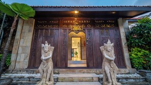 A villa entrance with ornate wooden doors, a stone pathway, and two stone statues. - Tropical Villa Asmara (Ungasan)