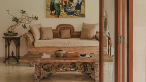 A living room with a sofa, a coffee table, a painting on the wall, and a door with a curtain. - Tropical Villa Asmara (Ungasan)
