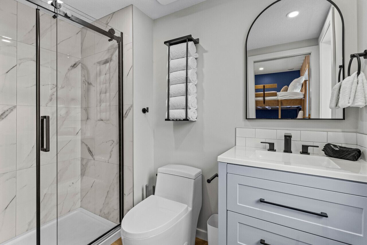 A modern bathroom with a glass shower enclosure, a white toilet, a vanity with a mirror, and a towel rack.