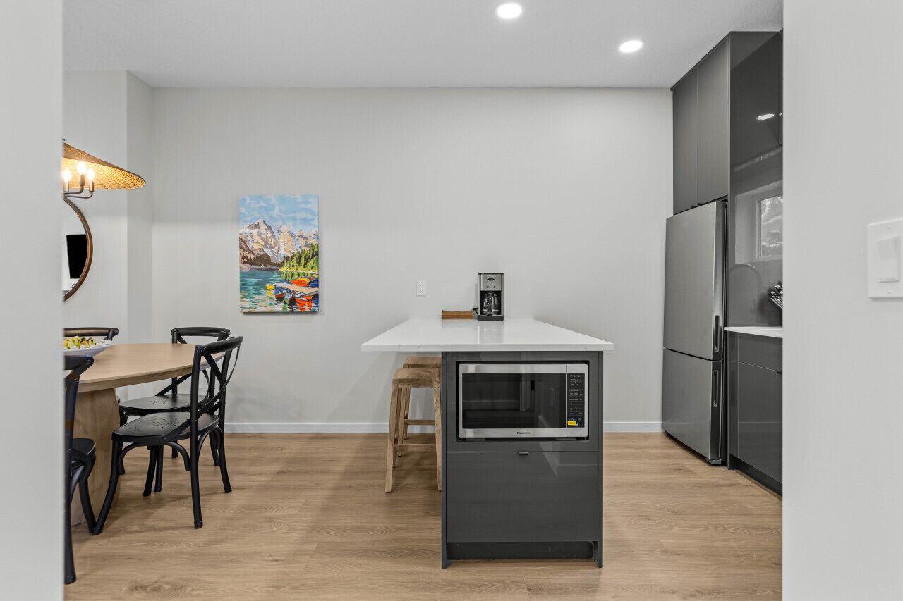 Una cucina compatta con un piano di lavoro bianco, un forno a microonde integrato e un frigorifero in acciaio inossidabile.